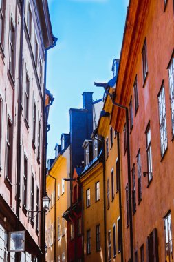 Aşağıdan rahat dar Ortaçağ sokak parlak mavi gökyüzü ve güneş ışınları arka planda Gamla stan, eski Stokholm şehir, İsveç bağlı sarı turuncu kırmızı binalar cephe ile görüntüleyin
