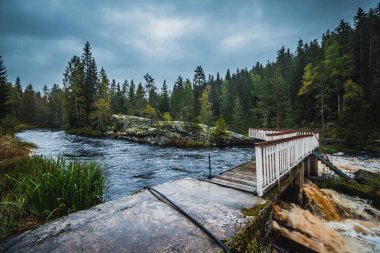 Nehir üzerindeki ahşap beyaz köprü Ormanın arasında, Karelia 'da çim ve taşlar