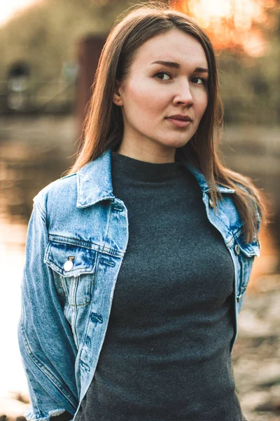 Портрет привлекательной, стройной, красивой молодой белокурой девушки в джинсовой куртке. Улыбающаяся девушка наслаждается теплой солнечной погодой в лесу — стоковое фото