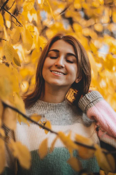 Šťastná dívka v teplém svetru stojí na podzimní žluté listy. — Stock fotografie