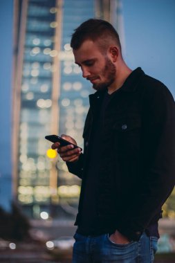 Akıllı telefon mesajları kullanan bir adam. Erkek, akşam saatlerinde şehirde cep telefonuyla taksiyi ya da uber 'i bekliyor. Genç işadamı cep telefonuna bakıyor.