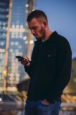 Akıllı telefon mesajları kullanan bir adam. Erkek, akşam saatlerinde şehirde cep telefonuyla taksiyi ya da uber 'i bekliyor. Genç işadamı cep telefonuna bakıyor.