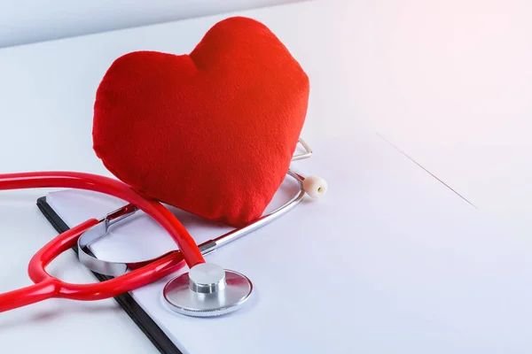 Red heart and stethoscope with empty clipboard on white table with copy space