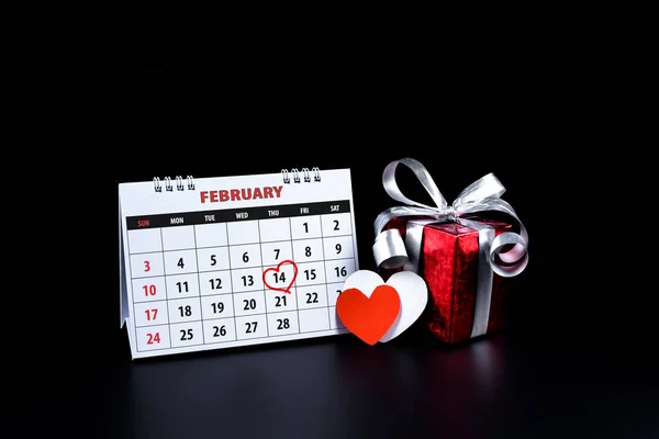 日历与红色写的心亮点2月14日的圣情人节提醒情侣表达爱与心脏形状 礼品盒在黑色背景 情人节的概念 — 图库照片