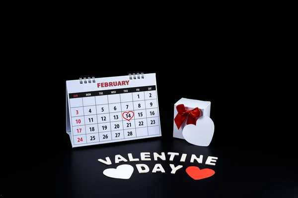 Calendar with red written heart highlight on February 14 with heart shape and gift box, Wooden letters word \