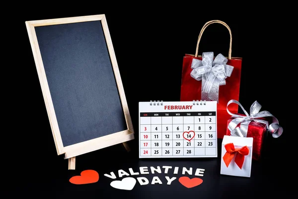 Calendar with red written heart highlight on February 14 with Empty chalkboard, heart shape and gift box, Wooden letters word \