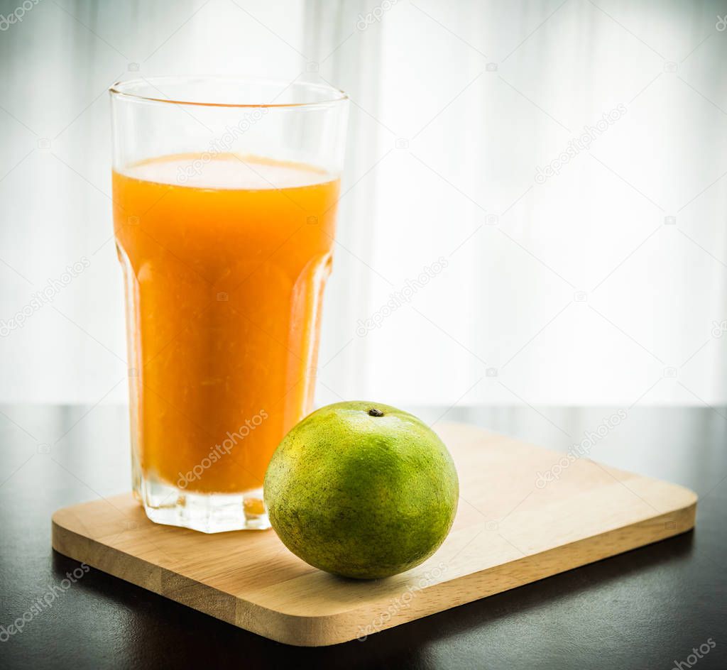 Glass of freshly pressed orange juice with orange on wooden table