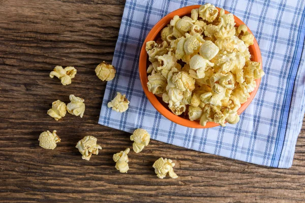 Homemade Sweet caramel popcorn in a bowl on blue cotton napkin against wooden background