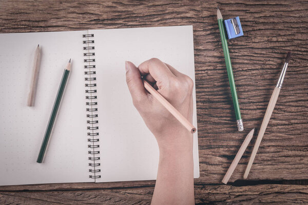 Human hands with pencil writing on paper on wooden table background