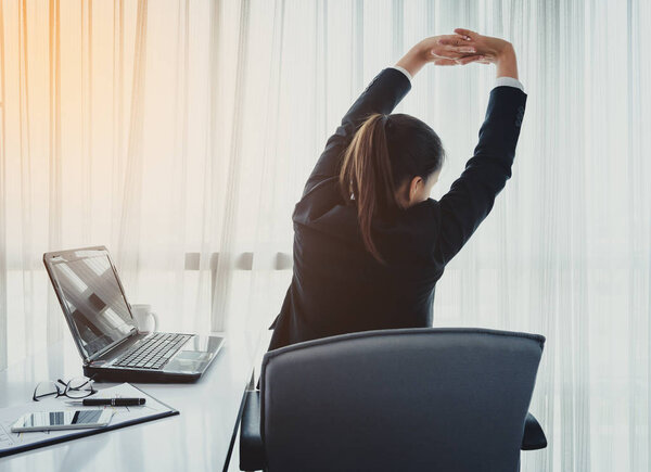 Successful businesswoman relaxing in her chair at the office with her hands clasped and stretch oneself. back view