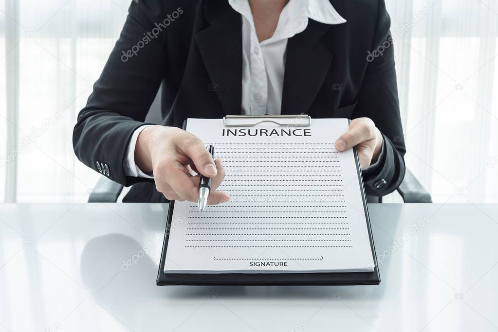 young woman in suit in his office showing an insurance policy and pointing with a pen where the policyholder must to sign