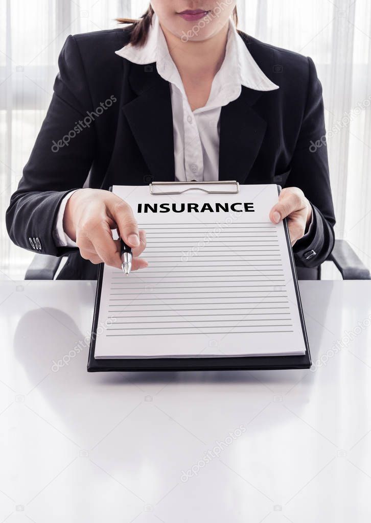 young woman in suit in his office showing an insurance policy and pointing with a pen where the policyholder must to sign