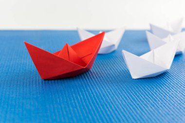 Beyaz ve mavi arka plan arasında önde gelen kırmızı kağıt gemi ile liderlik kavramı