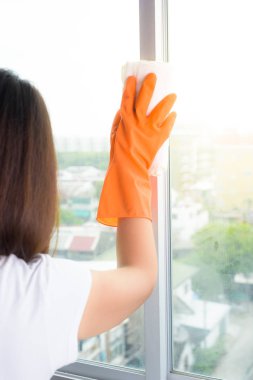 Happy Asian woman in gloves cleaning window with rag and cleanse clipart