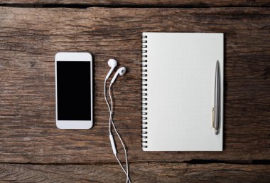 Kalem, not defteri, akıllı telefon ve kulaklık ile ofis ahşap büro. 