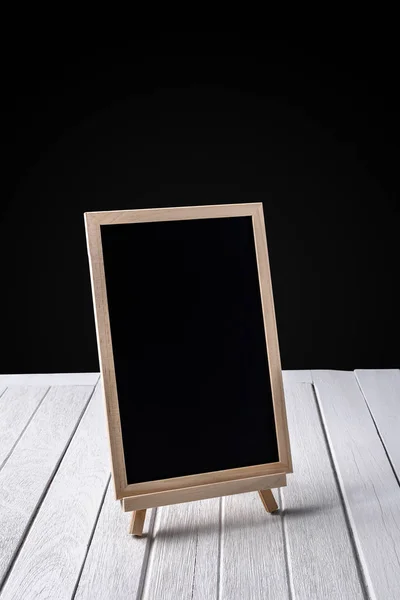 The chalkboard on the stand on wooden floor and black background