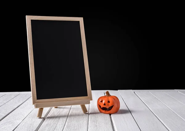 The chalkboard on the stand with Halloween Pumpkins on wooden fl