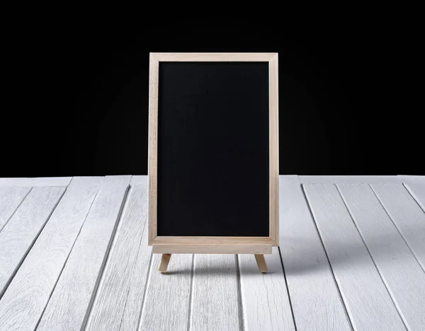 The chalkboard on the stand on wooden floor and black background