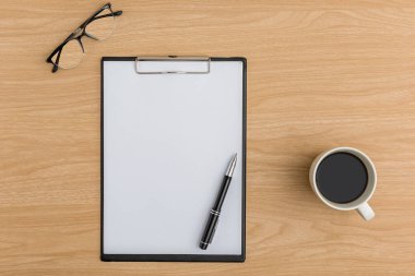 Üst kat ofis masası. Boş pano, kalem, gözlük, kahve fincanı ofis malzemeleriyle ahşap masa arkasında düz bir çalışma alanı..