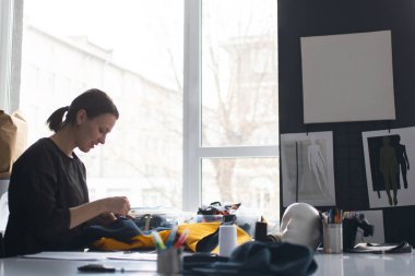 Dikkate değer çekici genç kadın terzi ayakta duruyor ve tekstil malzemelerini çiziyor. 