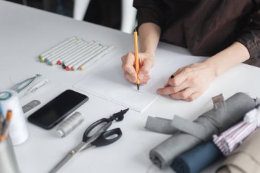 Terzilik işyeri. Terzi eskiz çizgilerindeki kıyafet detaylarını kesiyor. 