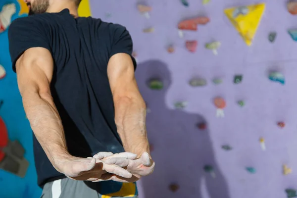 Güçlü ve kaslı bir sporcu yapay bir duvara tırmanmaya hazırlanıyor.