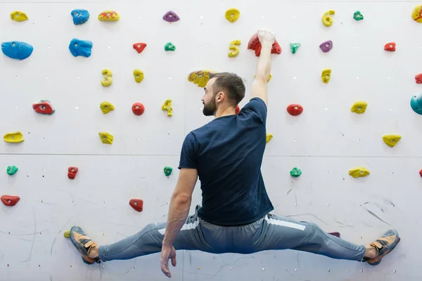 Сильный и мускулистый альпинист, занимающийся спортом в тренажерном зале на искусственной стене, окрашенной в белый цвет — стоковое фото
