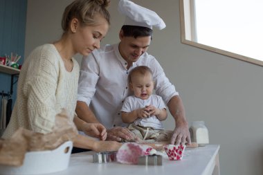 Aile aşçıdır. Oğlum, anne ve baba hamur tozu hazırlayın. Hepsinde önlük var. Evinde, mutfakta yaşa. Eğleniyorlar ve gülümsüyorlar.. 