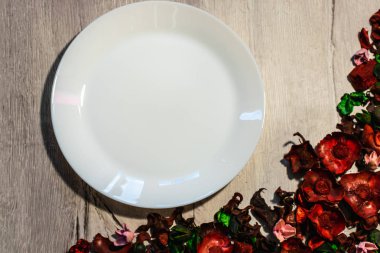 Ahşap arka plan boş beyaz tabakta kuru çiçek yaprakları ile süslenmiş. Yukarıdan görüntülemek.