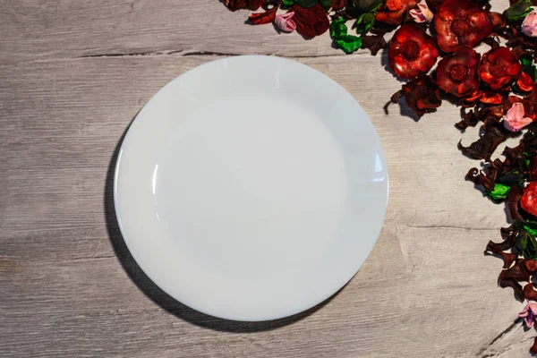 Ahşap arka plan boş beyaz tabakta kuru çiçek yaprakları ile süslenmiş. Yukarıdan görüntülemek.