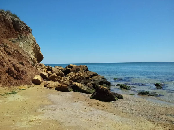 Kayalık ve yosun ve yosun ile taşlar sarı kum ve mavi berrak su ile vahşi plajda. Karadeniz.