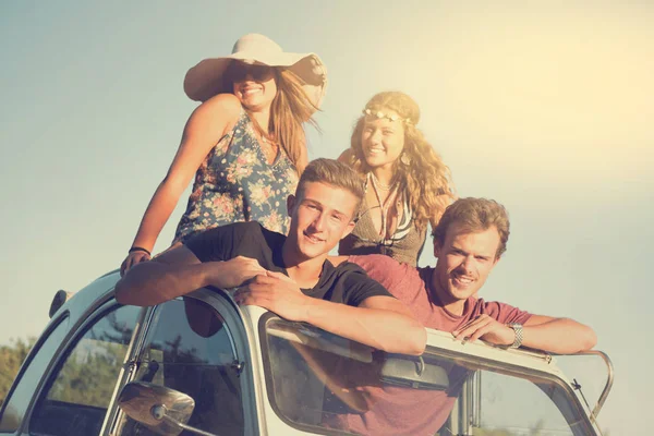 Group of happy people in a car at sunset in summer, ready for a roadtrip.