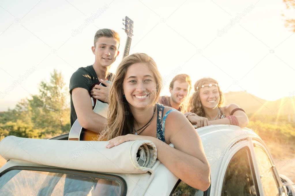 Group of happy people in a car at sunset in summer.