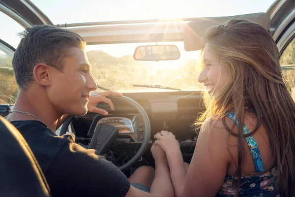 Happy young couple in a car enjoying the beautiful sunset in countryside.