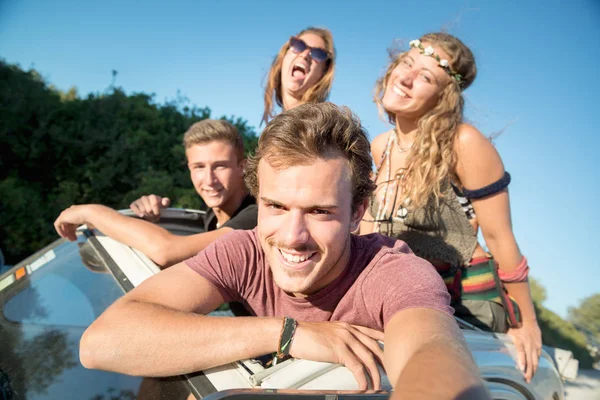 Group of happy people taking a selfie in a car at sunset in summer.