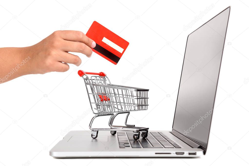 Laptop with small shopping cart and a hand with credit card isolated in white