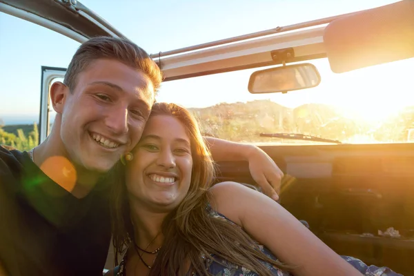 Happy young couple in a car enjoying the beautiful sunset in countryside.