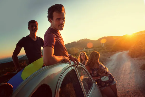 Group of happy people in a car at sunset in summer.