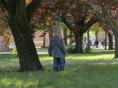 Prag, Çek Cumhuriyeti - 7 Mayıs 2018: Bahçede bir ağaç yakınındaki iki yaşında bir çocuk duruyor. Yakınındaki bir ağaç bahçe çim üzerinde sarışın bir çocuk duruyor.