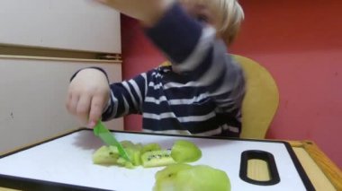 Bir çocuk bir meyve bir bıçakla kesiyor. Çocuk meyve tahtada bir bıçakla keser.