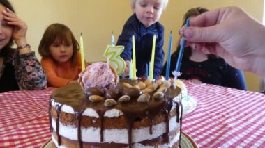 Kadın elleri mumlar ile Çikolatalı Kek süslüyor. Mum figürü üç yıl. Üç yıl Doğum günü. Masada çocuklar bir şenlikli kek bekliyor.