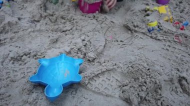 Üç yaşında bir çocuk kum havuzunda oynuyor. Rebony bahçede kumla oynuyor. Kum havuzunda çocuk oyuncakları var. Çocuk spatula ve kova.