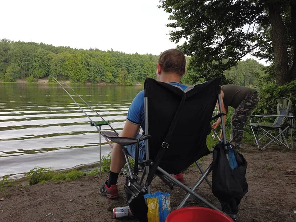 Un hombre con cañas de pescar en la orilla mientras pesca en un bosque l — Foto de Stock