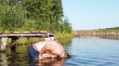 Bir adam kafasını gölde sulıyor. Bir adam göle dalıyor. Gün batımında su sıçrayan.