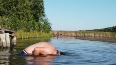 Bir adam kafasını gölde sulıyor. Bir adam göle dalıyor. Gün batımında su sıçrayan.