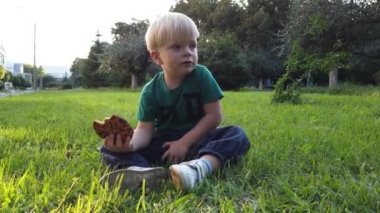 Çocuk yeşil bir çimenlikte oturan kurabiye yiyor..