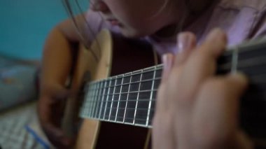 Çocuklar gitar çalmayı öğrenirler. Bir gitarın ve çocuk eli tellerin yakın çekimi..