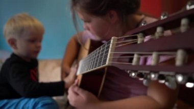 Çocuklar gitar çalmayı öğrenirler. Bir gitarın ve çocuk eli tellerin yakın çekimi..