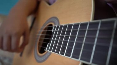 Çocuklar gitar çalmayı öğrenirler. Bir gitarın ve çocuk eli tellerin yakın çekimi..