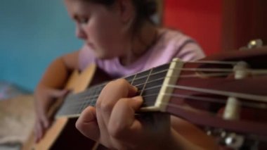 Çocuklar gitar çalmayı öğrenirler. Bir gitarın ve çocuk eli tellerin yakın çekimi..